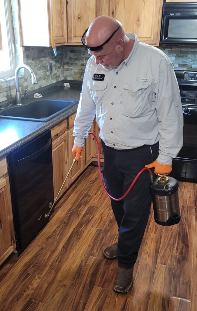 Pest control technician applying indoor treatment along kitchen cabinets